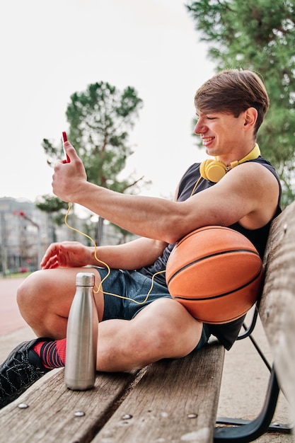 Basketball player resting male athlete sitting while making a video call on his mobile phone