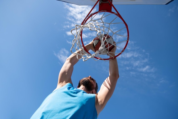 Basketball player. sports and basketball. a young man jumps and\
throws a ball into the basket. blue sky and court in the\
background.