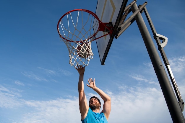 バスケットボール選手スポーツとバスケットボール若い男がジャンプしてバスケットにボールを投げる青い空と背景のコート