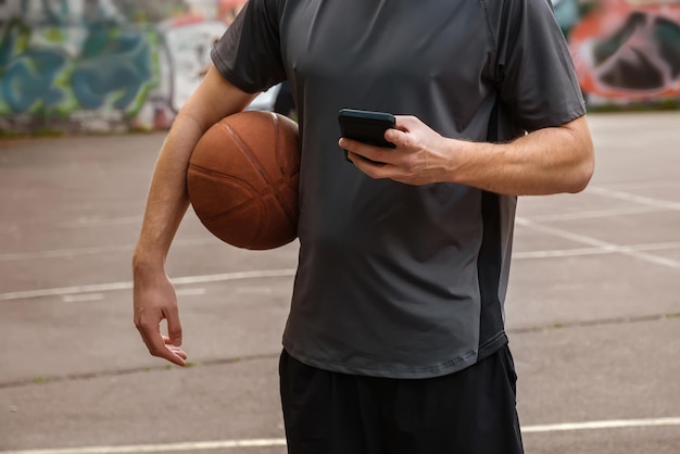 Basketball player with ball and phone in hands on open basketball court