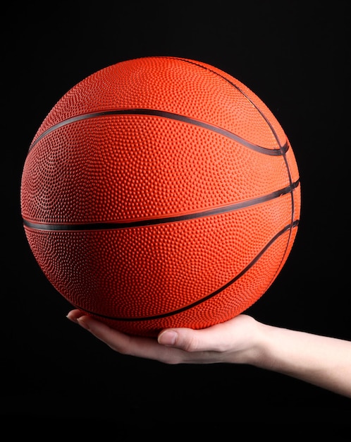 Basketball in woman hand on black background