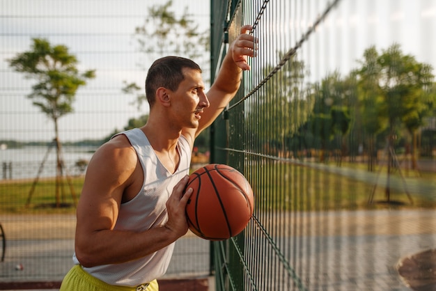 Basketbalspeler die zich bij het gaasomheining bevindt