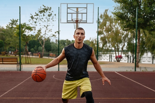 Basketbalspeler met bal in beweging op buitenbaan.