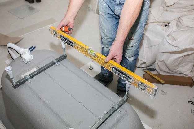 Bath installation Worker is making measures with spirit level Maintenance repair in the flat Renovation process