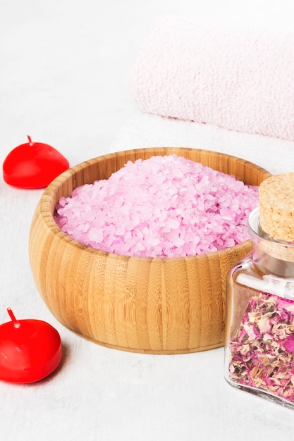 Photo bath salt with aroma of a rose in a wooden bowl, petals and a fresh pink rose, towels and candles on a white background