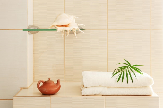 Банные полотенца, ракушка и керамический чайник в интерьере ванной комнаты