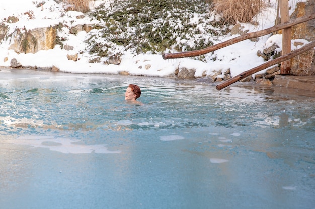 Bathing young woman in a frozen lake after sauna.