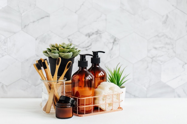 Bathroom accessories, natural cosmetics products and tools with\
green plant on white table inside a bathroom background.