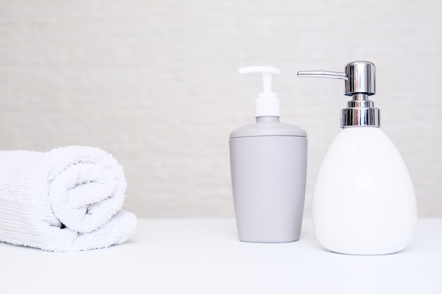 Bathroom background, toilet accessories for hand and body care, liquid soap dispenser and towels against light background.