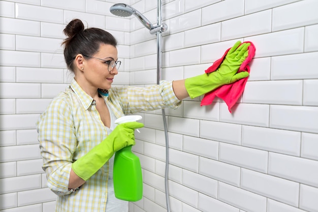 Foto pulizia del bagno, casalinga che lava il muro di piastrelle bianche con detersivo e straccio, copia spazio. igiene, purezza, concetto di pulizia