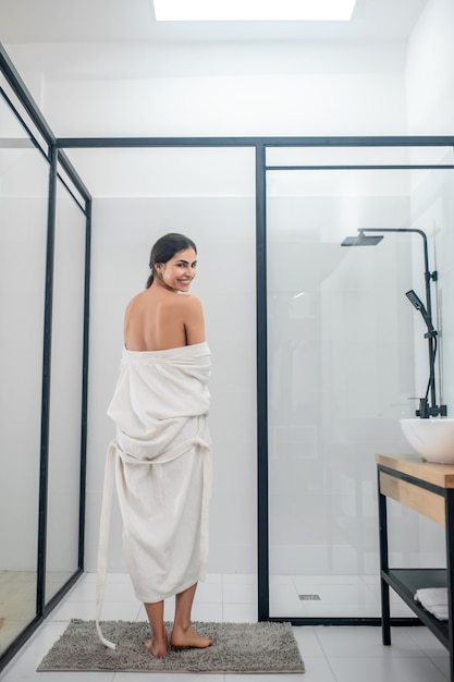 In the bathroom. A dark-haired young girl in a white bathrobe in the bathroom