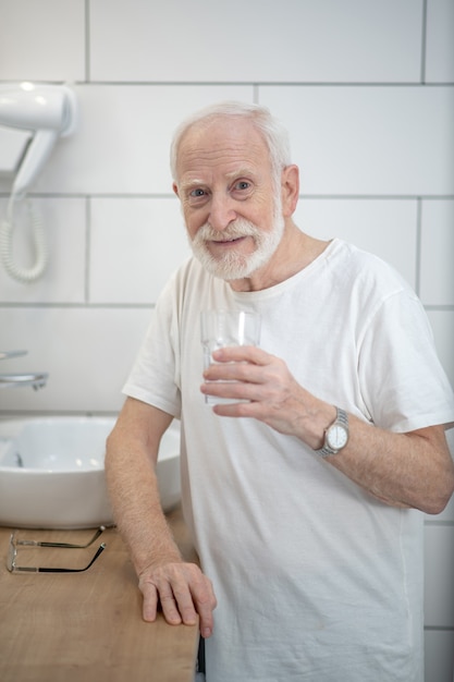 In the bathroom. Gray-haired man in white tshirt in the bathroom