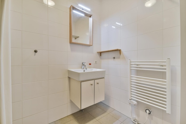 Интерьер ванной комнаты, отделанный белой плиткой, с раковиной под зеркалом в современном доме