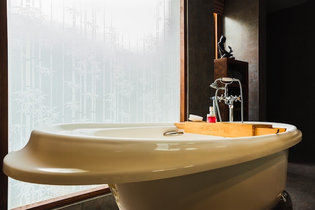 Интерьер ванной комнаты класса люкс в современном стиле с ванной и окном.