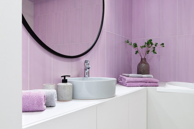 Interno del bagno in stile minimalista con piastrelle rosa, specchio rotondo sopra il lavandino e asciugamani.