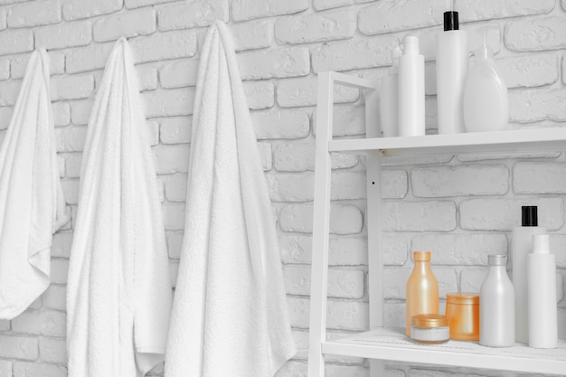 Bathroom shelving with cosmetic bottles and white hanging towels against white brick wall