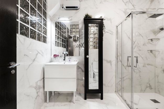 유리 파티션 프레임리스 직사각형 거울이 있는 샤워 캐빈이 있는 욕실, 거울과 조약돌 벽과 결합된 회색 줄무늬 대리석 클래드 벽이 있는 긴 검은색 나무 캐비닛
