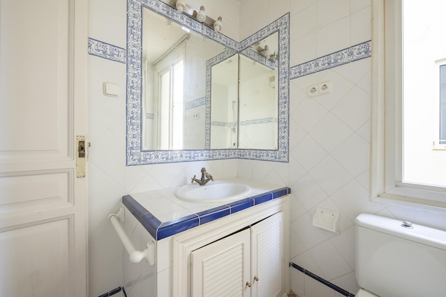 Bathroom with vintage style white tiles with blue borders and blue patterned borders surrounding the mirror and brass taps