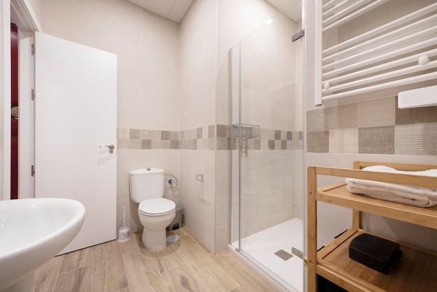 Ванная комната с белой фарфоровой раковиной, квадратной душевой кабиной со стеклянной дверью, полотенцесушителем и полкой из бамбукового дерева.