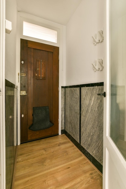 A bathroom with wood flooring and marble tiles on the walls along an open door leading to a bath room