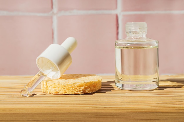 Bathroom wooden shelf with glass cosmetic bottle of yellow oil serum with pipette on a pink tile wall tile morning skin care ritual eco friendly sustainable beauty product copy space