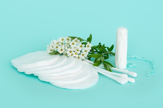 batons and cotton buds for ears and makeup remover made of cotton on a turquoise background with small white flowers.