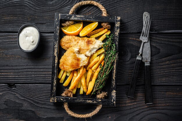 Battered Fish and chips dish with french fries and tartar sauce in a wooden tray