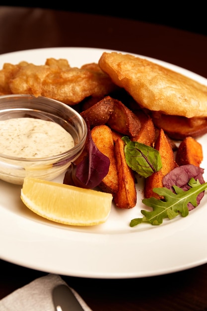 Battered fish on a plate with chips on a wooden table in pub unhealthy food