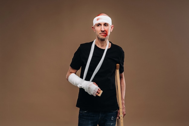 Battered man with a bandaged head and a cast on his arm stands on crutches