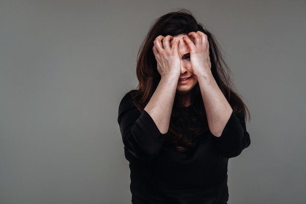 A battered woman in black clothes on an isolated gray background. Violence against women.