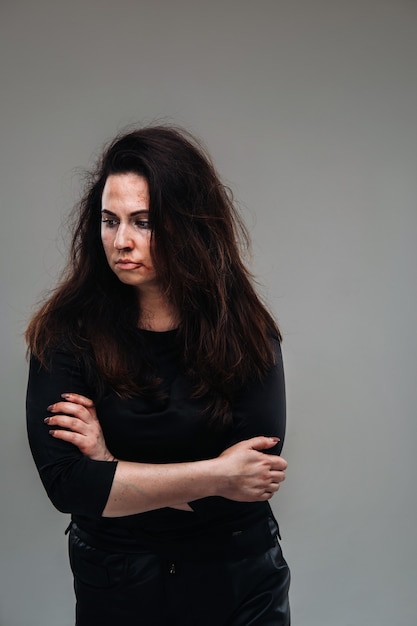 A battered woman in black clothes on an isolated gray background. Violence against women