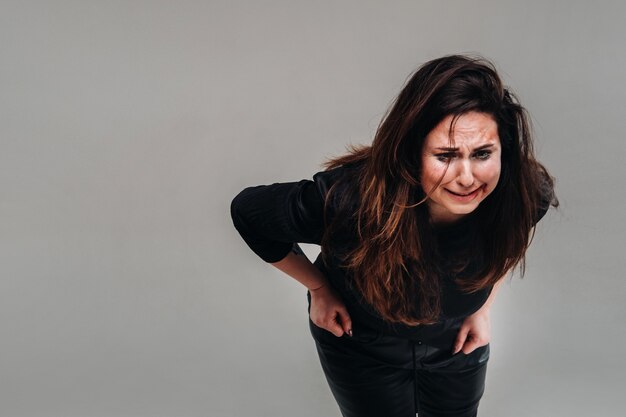 A battered woman in black clothes on an isolated gray background. Violence against women