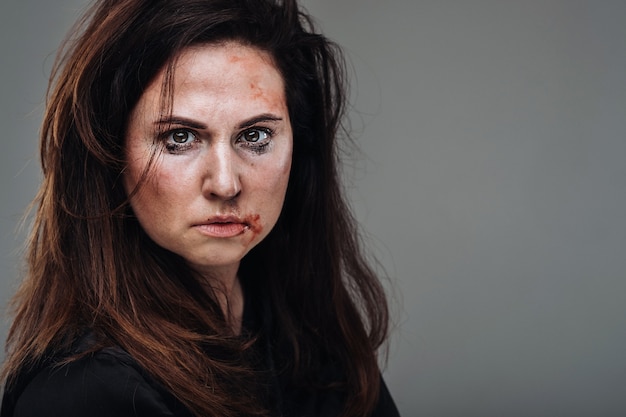 A battered woman in black clothes on an isolated gray wall. Violence against women.