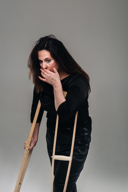 A battered woman in black clothes with casters in her hands on a gray background