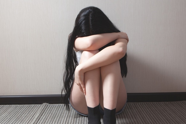 Battered young woman sitting near wall