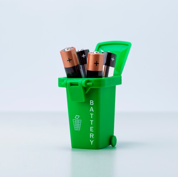 Batterijen in groene plastic container op lichtgrijze achtergrond. Batterijen giftig afval recycling en ecologie kwesties concept.