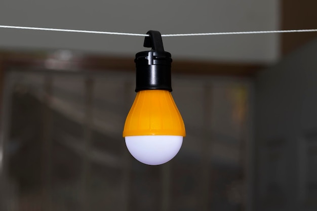 Photo a battery-backed lamp, lit and suspended on a wire with its hook.