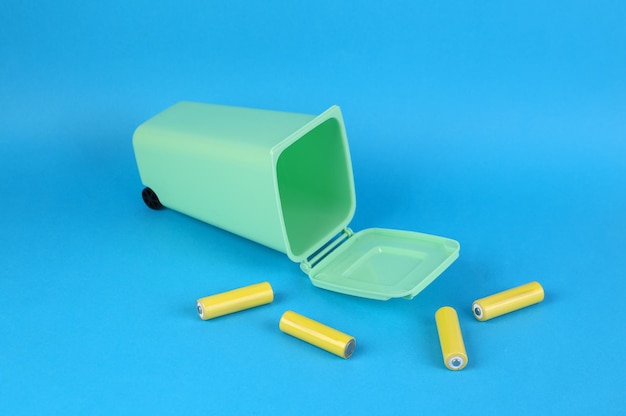 Battery recycling concept miniature trash can with aa batteries on blue background