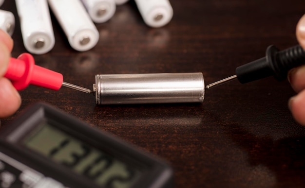 battery with volt calculator voltmeter red positive pole black negative pole on wood work table