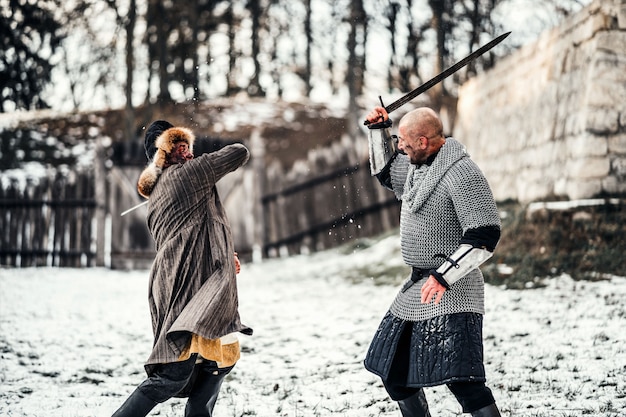 Battaglia di due guerrieri in armatura con armi che combattono con le spade nella neve