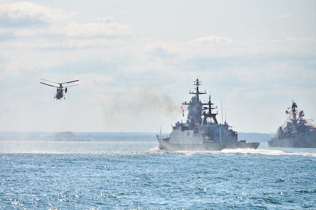 Battleships war ships corvette during naval exercises and helicopter maneuvering over water in Baltic Sea. Warships, helicopters and boats perform tasks in sea, military warships sailing, Russian Navy