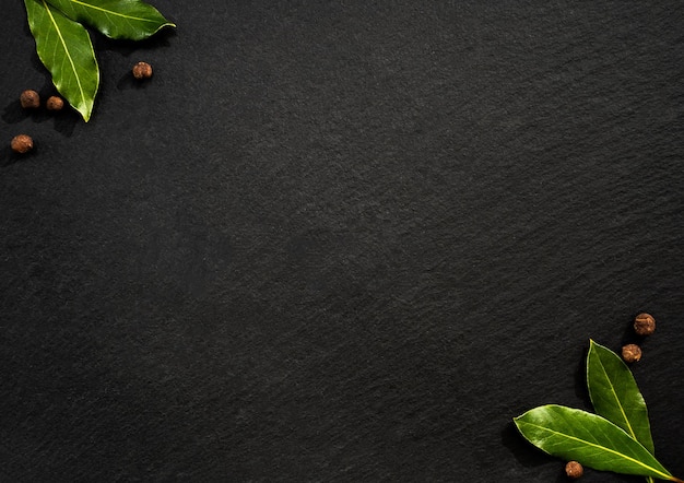 bay leaf and black pepper on a black background condiments flat view space for text