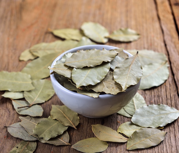 Bay leaves in white ceramic bowl on wooden table