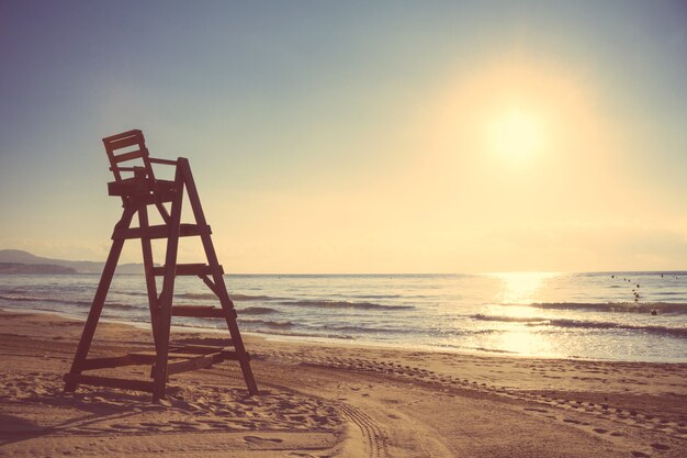Стул Спасателей Малибу на красивом пляже, пустом на летнем закате. Издание в мягких и теплых тонах.