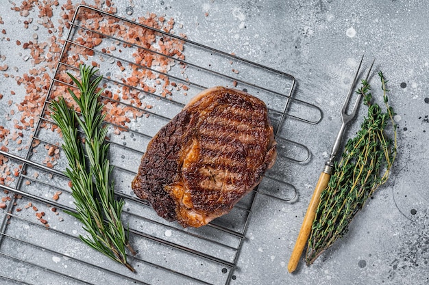 BBQ gegrilde ribeye steak rib eye rundvlees op een grill met kruiden Grijze achtergrond bovenaanzicht