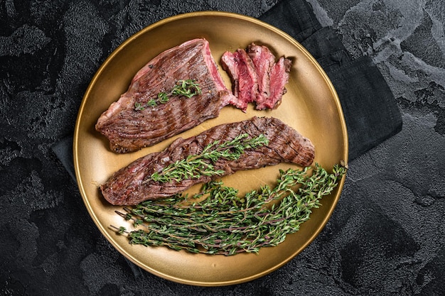 BBQ grilled Bavette Bavet beef meat steak with herbs on a plate Black background Top view