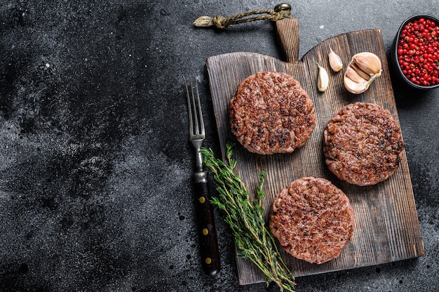 木の板にミンチ肉とハーブを使ったハンバーガー用のバーベキューグリルビーフミートパテ。黒の背景。上面図。スペースをコピーします。