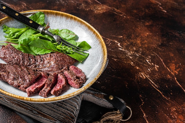 BBQ Grilled flank and Machete skirt steak in plate with vegetable salad. Dark background. Top view. Copy space.