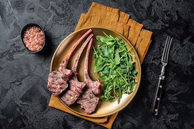 BBQ grilled lamb cutlet or mutton chop steak with arugula salad on a plate Black background Top view