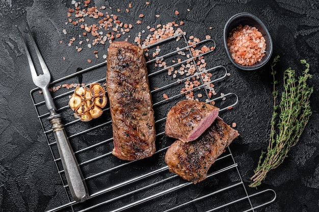 BBQ grilled Lamb tenderloin fillet meat on grill, mutton loin steak. Black background. Top view.